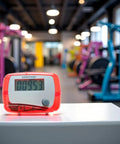 Red Portable Mini Digital LCD Pedometer That Tracks Steps Distance Calories Burned Exercise Time And Daily Target With Accurate Sensor Tech For Walking Running And Fitness On The Go on gym table