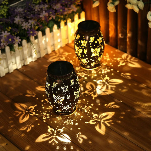 Butterfly Solar Powered Outdoor Metal Lanterns Set Of 2 Waterproof Hanging Patio Lights casting shadows on wooden deck.