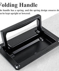 Black folding handle with spring mechanism, shown upright on a gray surface, used for recessed lift pull design