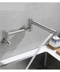 Foldable Wall-Mount Kitchen Faucet - Brushed Stainless Steel, water flowing into sink with modern design and sleek finish.