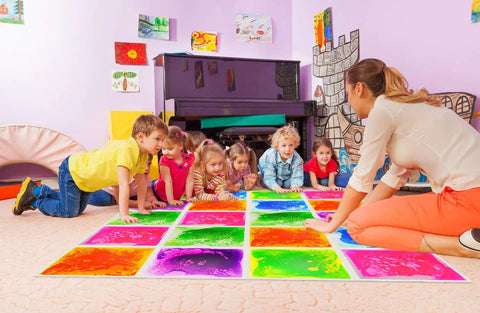 Children playing on Six Assorted Color 12 by 12 Inch Liquid Floor Tiles Set for Kids in a playroom, tiles changing color with movement.