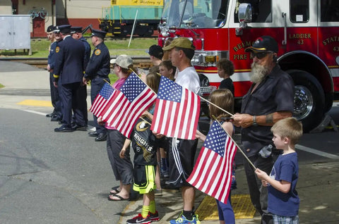 Children and adults holding 12 Pack USA Handheld Stick Flags 8 By 12 Inch Spearhead Patriotic American Flags Made In USA at a parade