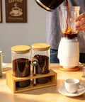Two 49oz Airtight Glass Coffee Canisters With Bamboo Shelf, Stainless Spoon And Anti Slip Pads for Storage Jars next to coffee maker