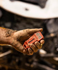 Close-up of red SuperATV winch remote control held by muddy hand