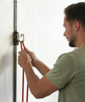 User attaching red resistance bands to Space Saving Wall Mount Gym Anchor System for workouts.