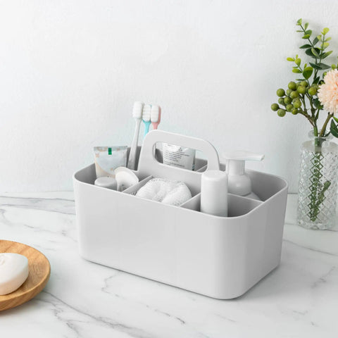 Gray all in one multipurpose caddy organizer with handle, visible compartments holding toiletries on a bathroom countertop.