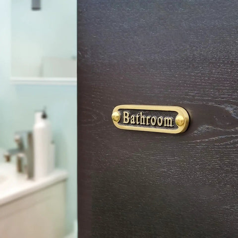 Brass bathroom door sign on dark wood, handcrafted metal decor