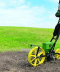 Person using 3lb Garden Seeder Workhorse with 7 seed plates for precise planting in prepared soil, sweet corn planter, wide rear wheel