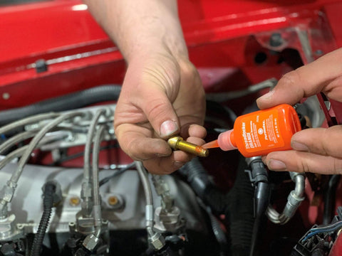 Orange Hybrid Strength Removable Threadlocker For High Torque Hold Delivers Three Times The Prevailing Torque Of Blue Threadlocker While Still Allowing Fasteners To Be Disassembled Perfect For Prolonged Vibration And Heavy Duty Assemblies 10 Ml being applied to engine bolt
