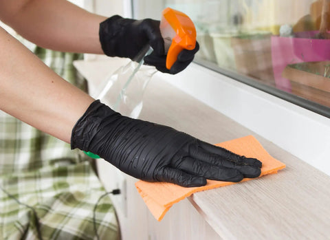 Person wearing Heavy Duty 6 Mil Nitrile Gloves Disposable Powder Free Exam And Work Gloves Latex Free Chemical Resistant Food Safe Medical And Mechanic Ready For Tough Jobs Black Large 100 Count while cleaning a surface with a spray bottle and cloth.
