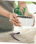 Multipurpose Manganese Grass Sickle With Handle Ergonomic Gardening Tool resting on table near person holding plant pot