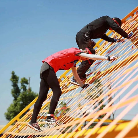 Individuals climbing a vertical obstacle using a Heavy Duty Cargo Net For Lifting And Securing Loads Tear Resistant Nylon Sling Net.