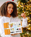 Happy person holding a wrapped 5-in-1 immersion blender set by the Christmas tree, featuring the Heavy Duty Immersion Blender Handheld Corded 1100W.