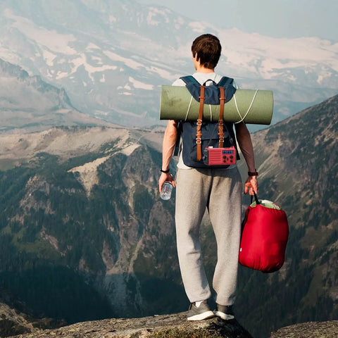 Hiker with red NOAA Weather Radio With Battery Backup And Solar Hand Crank, AM FM Shortwave Receiver in backpack, overlooking mountains