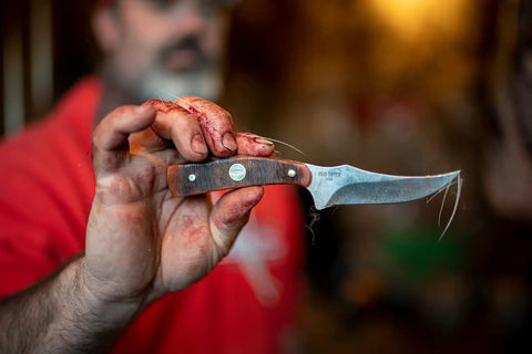 Generational USA Fixed Blade Knife With Three Point Five Inch Clip Point Skinner and stained hand close-up in outdoors setting.