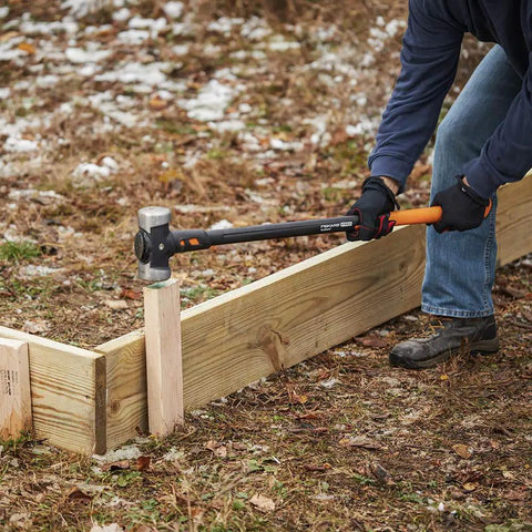 Person using IsoCore Shock Reducing 8 Pound Double Flat Face Sledge Hammer 36 Inch Beast Demolition Tool on wooden post outdoors.