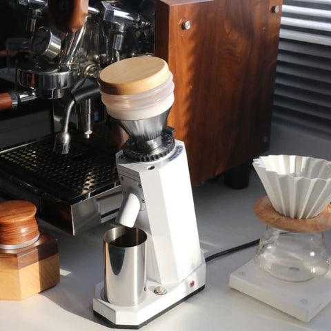 Kickstart Your Daily Grind With This Rock Solid Electric Coffee Grinder Featuring 40Mm Conical Titanium Burrs 19 Straight Forward Settings And A Generous 75G Bean Hopper. Image shows a white coffee grinder with wooden accents, a glass brewing setup, and a stainless steel cup.