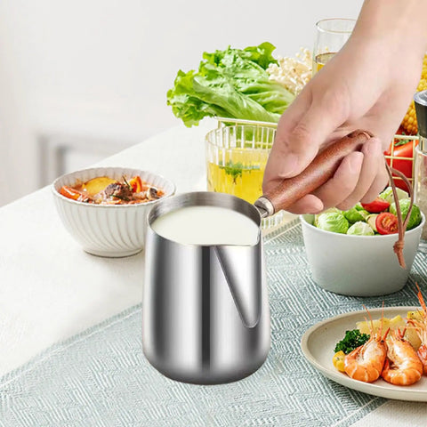 Person holding Stainless Steel Milk Warmer And Frother Pot With Wooden Handle Barista Grade Multipurpose Milk Frother Cup For Home Or Cafe 900ml Capacity Great For Latte Art Coffee Tea And Melting Chocolate