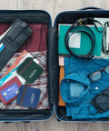 Open suitcase packed for travel with clothes, camera, and accessories laid out on a wooden floor.