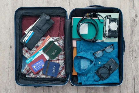 Open suitcase packed for travel with clothes, camera, and accessories laid out on a wooden floor.