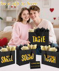 Five Senses Gift Bag Set For Him With Labels And Tissue Paper held by couple, medium black gift bags on sofa with sensory labels.