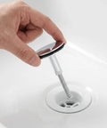 Hand holding Rotary Bath Tub Plug Drain Stopper for Bathtub Overflow Cover above a bathtub drain for easy installation.