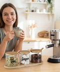 Woman enjoying coffee beside Three Pack Clear Glass Jars With Lids And Spoon On Bamboo Tray For Coffee Beans Sugar Tea