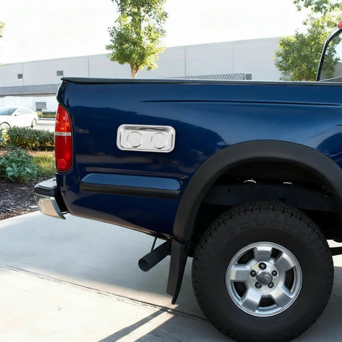 Blue pickup truck parked on driveway near green bushes with industrial buildings in the background