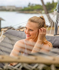 Woman relaxing on Two Person Outdoor Hammock With Stand And Carry Bag, Cotton Rope Hammock With Detachable Reversible Quilted Pad, Dark Gray.