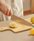Front view of a bamboo cutting board with handle on a countertop, knife slicing a lemon.