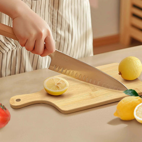 Front view of a bamboo cutting board with handle on a countertop, knife slicing a lemon.