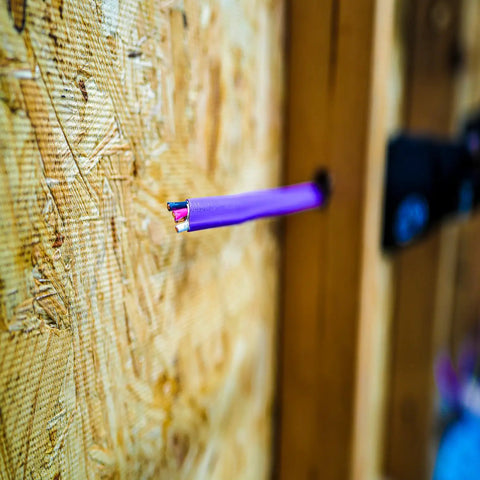 Close-up of Romex Simpull 12 Gauge 3 Conductor NM-B Solid Copper Indoor Cable With Ground protruding from wooden surface.