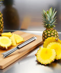 V Shape Pineapple Eye Remover Tool With Multipurpose Clip Stainless Steel Peeler next to sliced pineapple on a cutting board