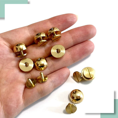 Top Shelf Solid Brass Bottom Guards For Handbags And Totes Round Screwback Feet 8 Pack shown in hand, including kickstands and screws.