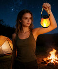 Woman holding USB Charging Solar Lantern For Outdoors And Travel at night, with tent and campfire in the background.