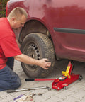 Man using lightweight 2 ton floor jack with carbon steel handle to lift car for tire change