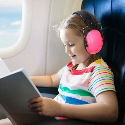 Child wearing pink earmuffs, part of 9 Pack Kids Earmuffs For Noise Reduction 29dB Adjustable Fit Ear Protection, reading on airplane.