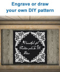 Front view of a black anodized aluminum engraving blank with a white floral border, framed in a wooden display