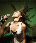 Woman singing energetically into a microphone with hair flowing, wearing a spiked choker and a white top in a music studio.