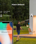 Dual Lens 1080P Outdoor Security Camera With Color Night Vision, Active Light And Siren Alarm, PIR Motion Detection, mounted on a house wall with a young man receiving alerts on his phone.