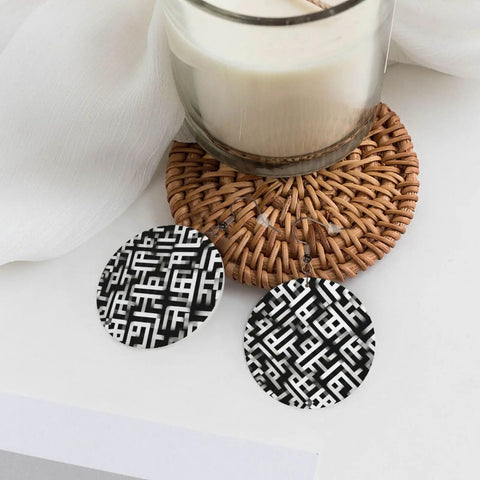 Black And White Grid Print Dangle Earrings For Women, Hella Lightweight Faux PVC Leather Look With Secure Silver Plated Hooks on a table with a candle.