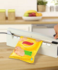 Heavy Duty Twelve Inch Impulse Bag Heat Sealer Constructed With Hella Rugged Aviation Aluminum Body For Badass Commercial Food Packaging And Secure Retail Storage in action sealing a snack bag.