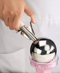 Hand using Thumb-Press Food Disher Ice Cream Scoop 4.67 Oz Size 6 White, 18/8 Stainless Steel, for portioning ice cream.