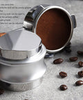 Dual Head Espresso Coffee Distributor And Adjustable Tamper With Bamboo Base Smoothly Fluffs And Levels Grounds For Dead Nuts Consistent Pulls In 51MM Portafilter Baskets on a gray surface with coffee beans.