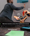 Man painting wall with roller, surrounded by spray paints, paint thinner, and a protective sheet on the floor, showing DIY setup.