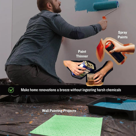 Man painting wall with roller, surrounded by spray paints, paint thinner, and a protective sheet on the floor, showing DIY setup.