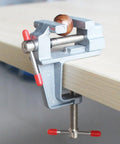 Built Tough Mini Table Vise Crafted From Premium Aluminum Alloy featuring wide flat jaws securing a wood piece on a workbench.