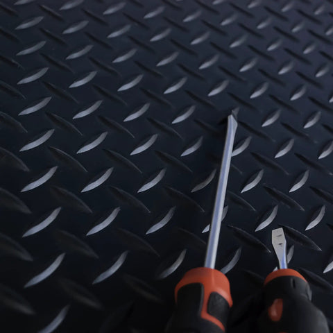 Close-up of Commercial Grade Vinyl Diamond Plate Floor Mat Knockout Traction with screwdrivers on a textured surface.