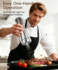 Sleek Stainless Steel Electric Salt And Pepper Grinder Set With Led Light, Adjustable Coarseness, Rechargeable Battery, Storage Base, Premium Automated Spice Mill For Modern Kitchen Gadgets in use over grilled steak.