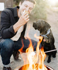 Man roasting marshmallows over Ranger Portable Outdoor Fire Pit With Stand Stainless Steel Firepot, dog watching nearby